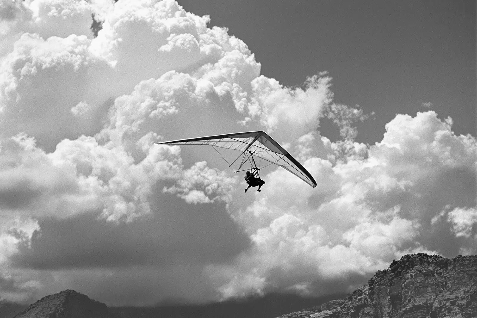 Ala delta planeando junto a una cresta rocosa frente a nubes de tormenta