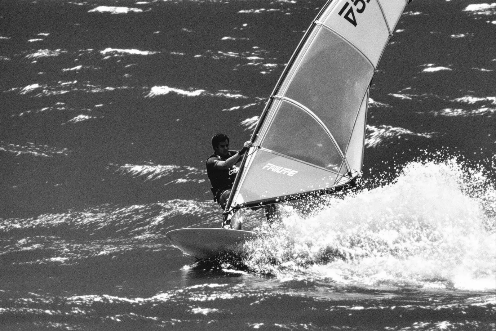 Windsurfista planeando con la vela cargada y una cortina de espuma detrás
